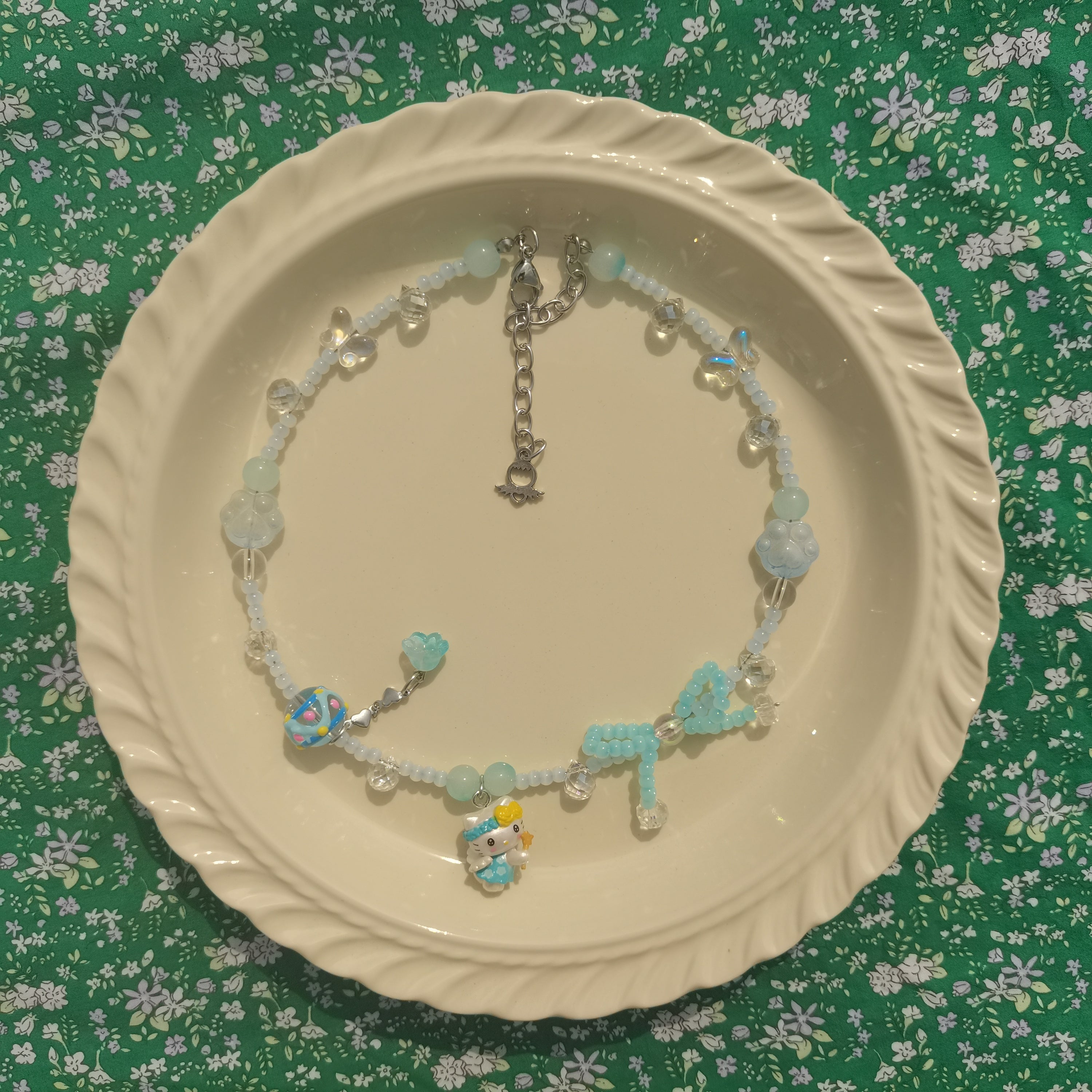 Artistic presentation of a Y2K fashion-inspired beaded necklace with Hello Kitty charm on a white surface