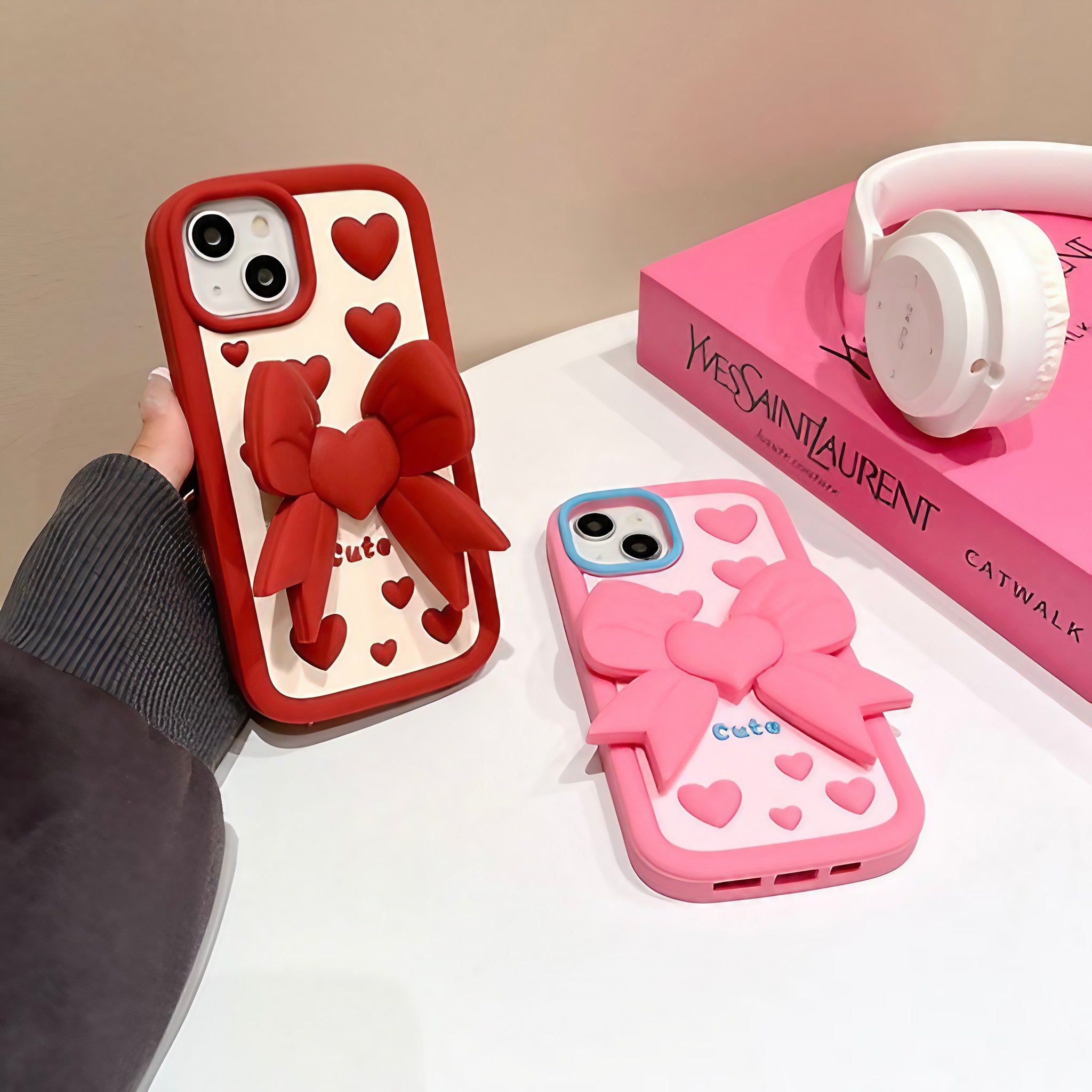 Pair of pink and red Coquette iPhone cases with heart designs and bow accents for various models