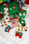 Festive holiday socks displayed with a Christmas tree and gifts on a cozy blanket