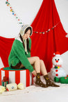 Woman in a green sweater relaxing on a candy cane-striped cushion, wearing cozy reindeer plush socks