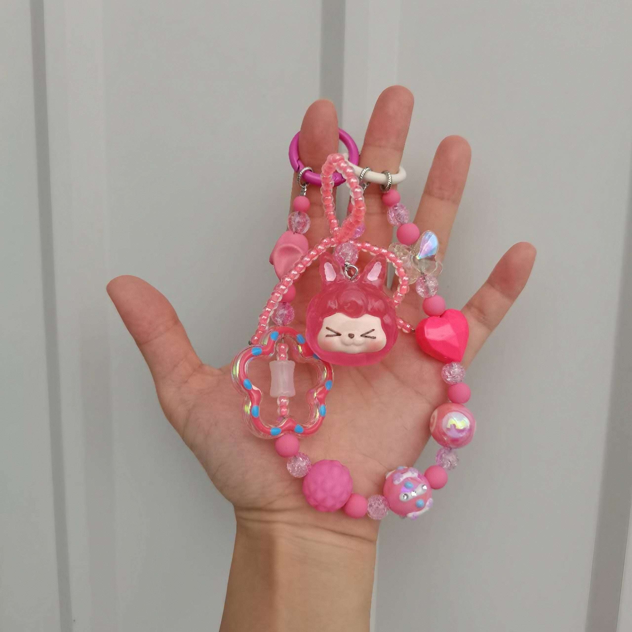 A hand displaying the Coquette Fashion Essential pink bag chain with pink beads