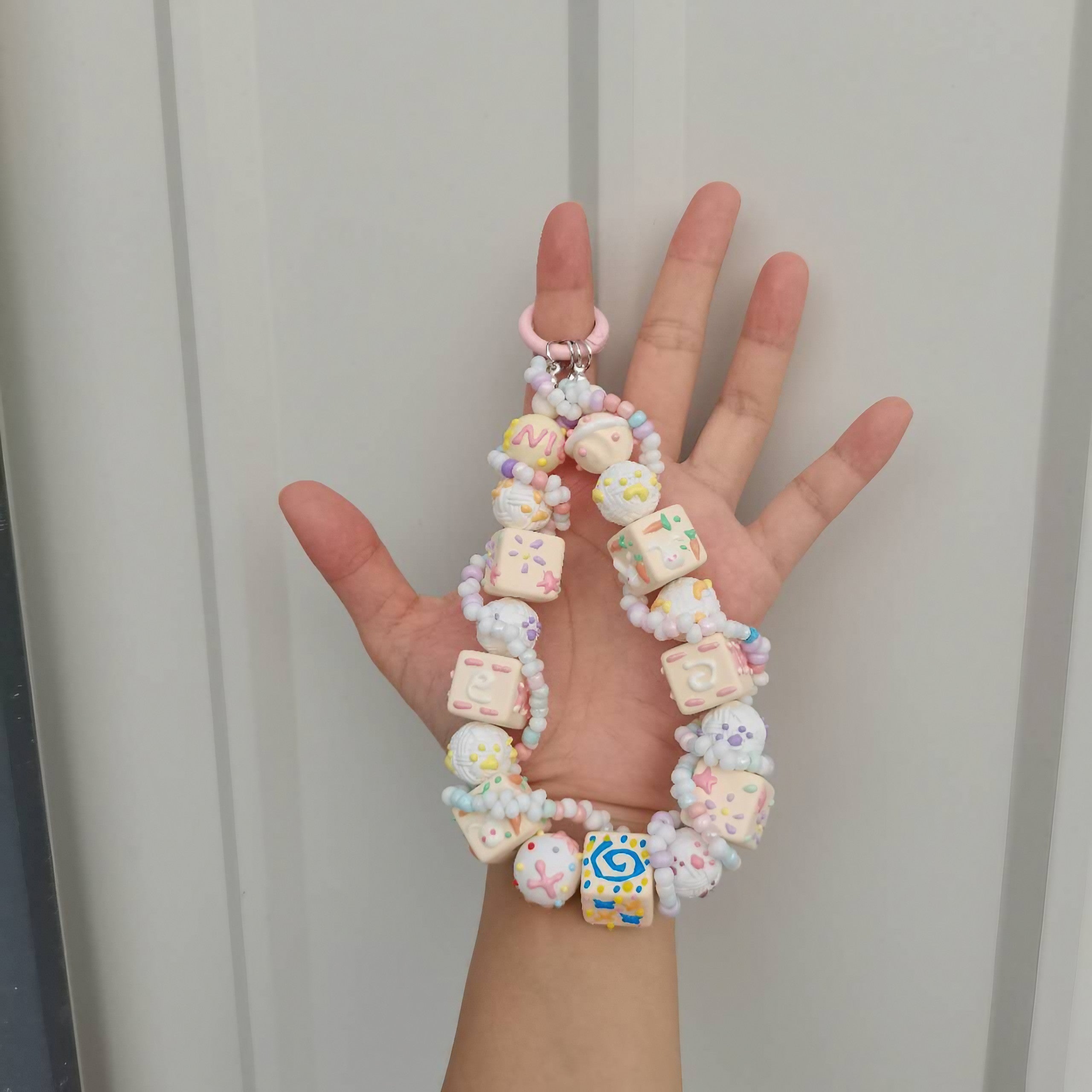A person holding a white keyring adorned with hand-drawn beads, suitable for an old money style look
