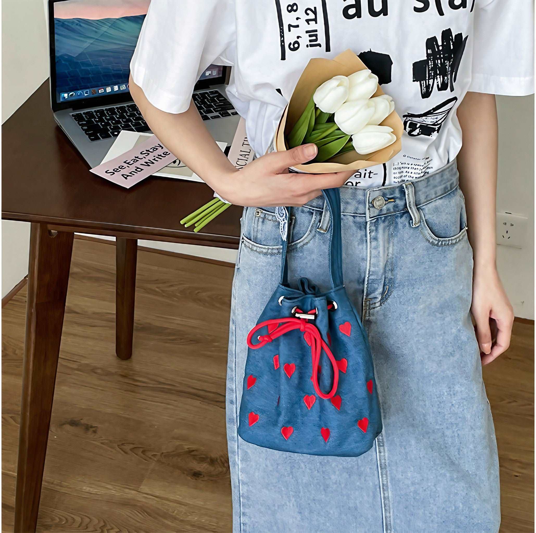 A woman presenting a blue denim heart bag while holding a flower