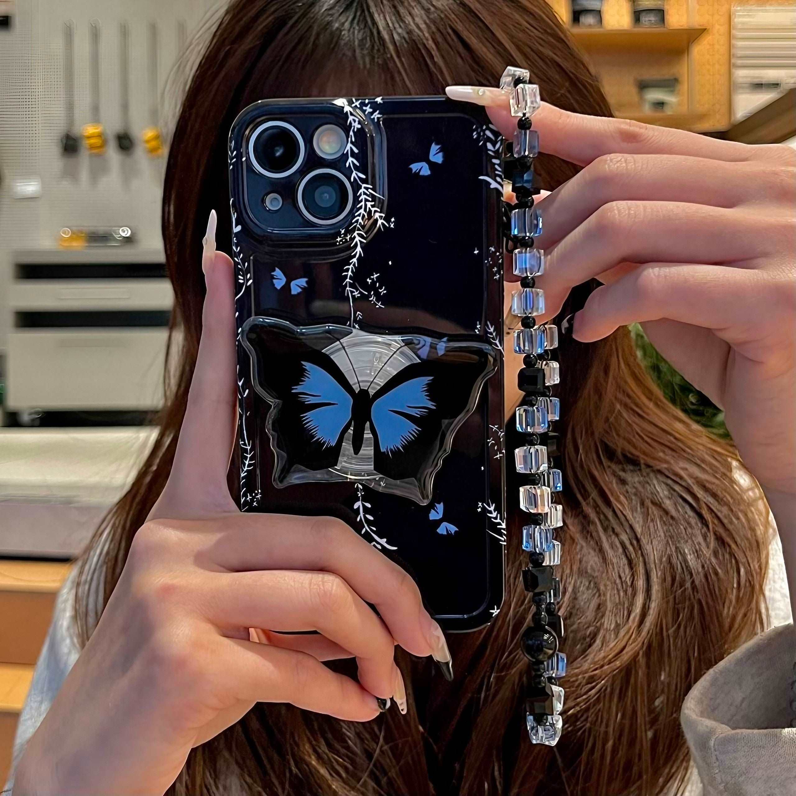 A hand showcasing a black iPhone case with a butterfly motif and matching phone stand and keyring