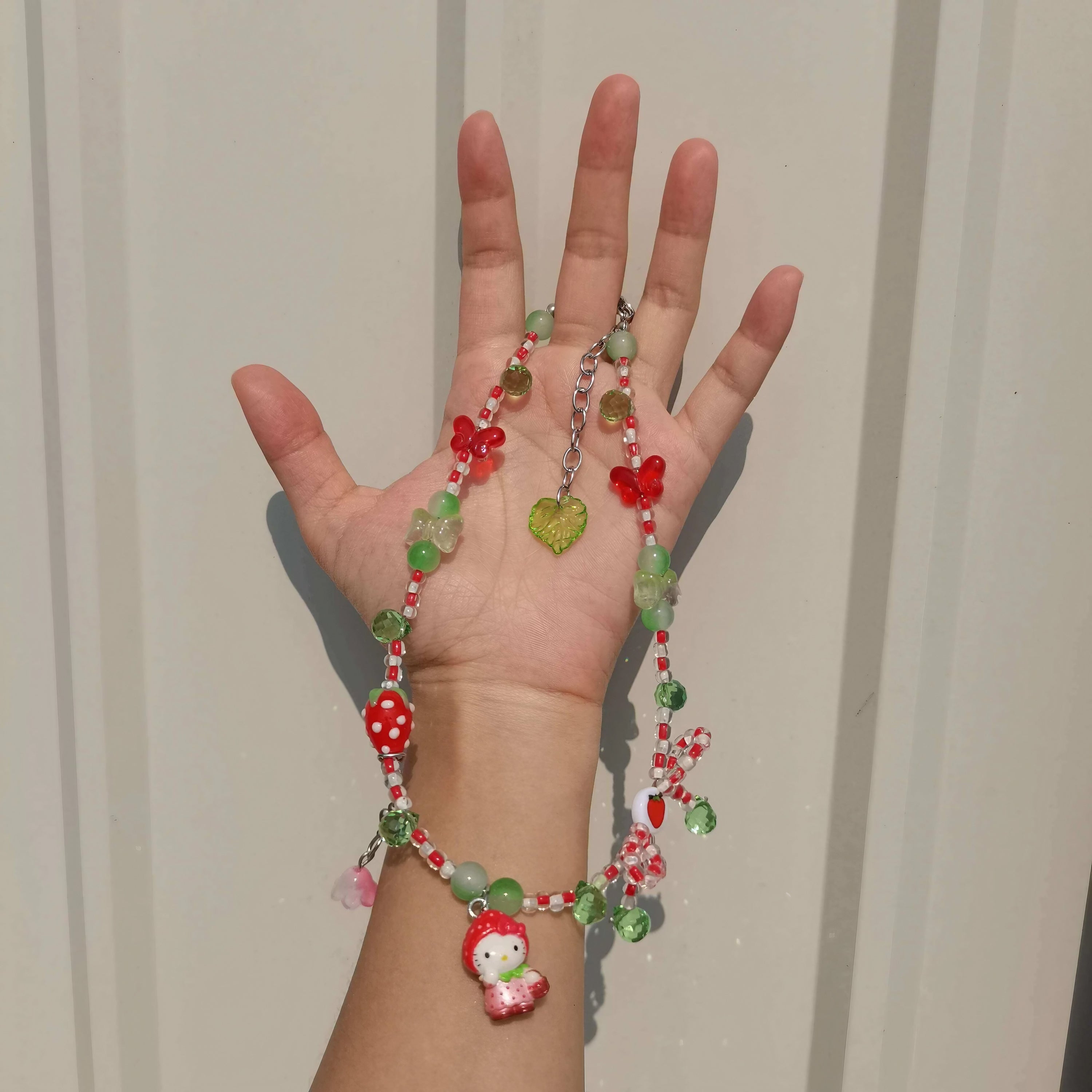 Close-up of a hand displaying a handmade red beaded Hello Kitty necklace