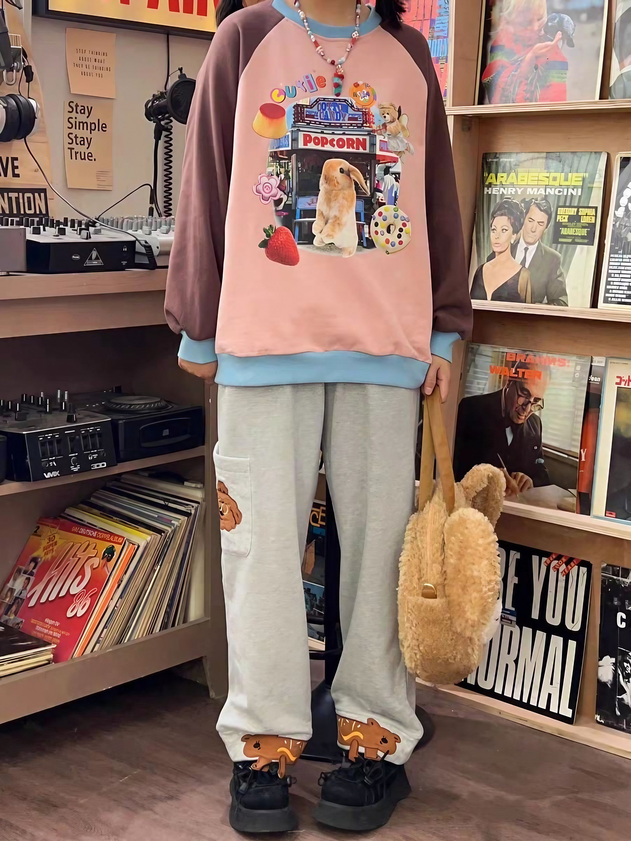 A stylish individual in a cartoon-themed sweatshirt paired with casual pants and holding a plush toy