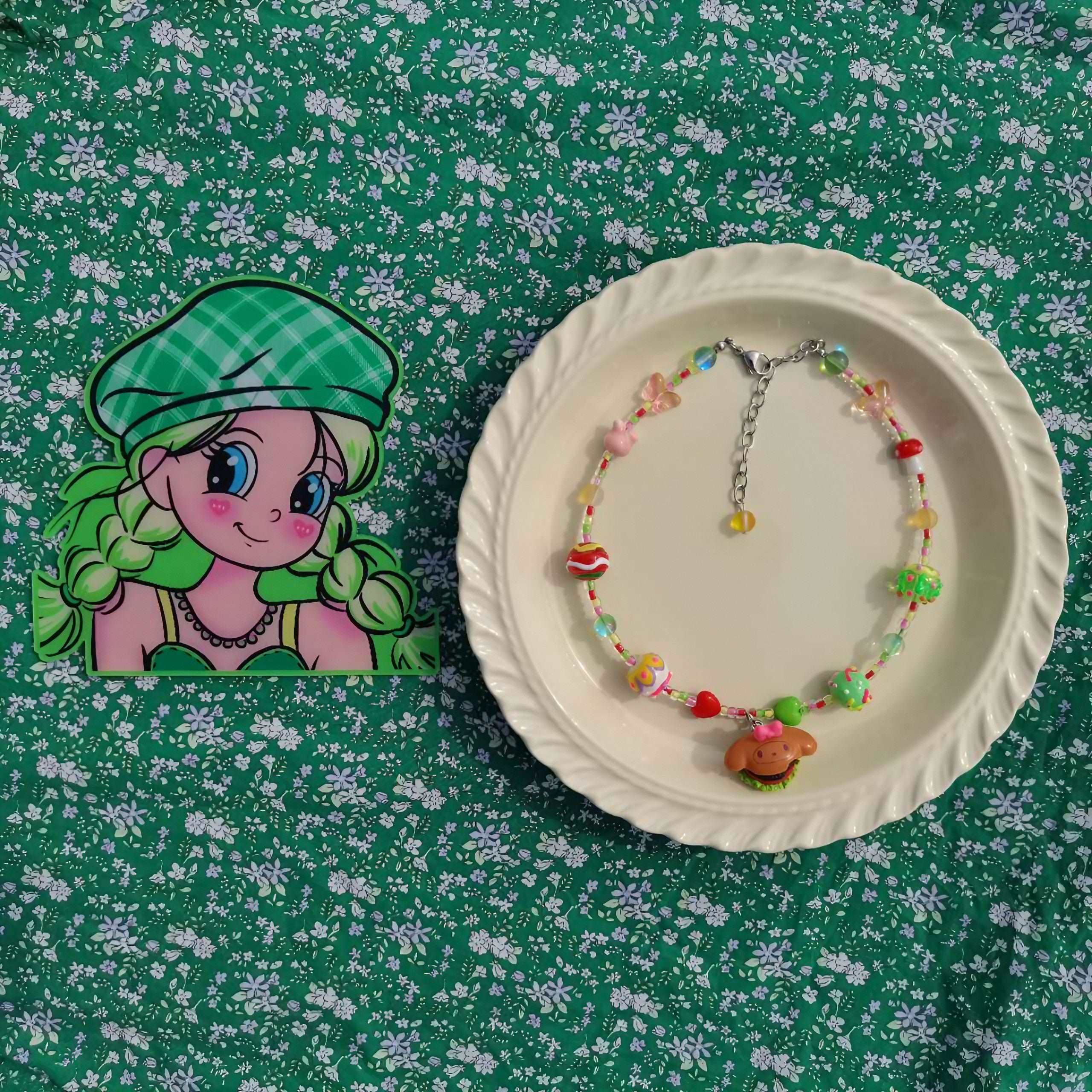 Autumn fashion themed necklace and green hat arranged on a plate