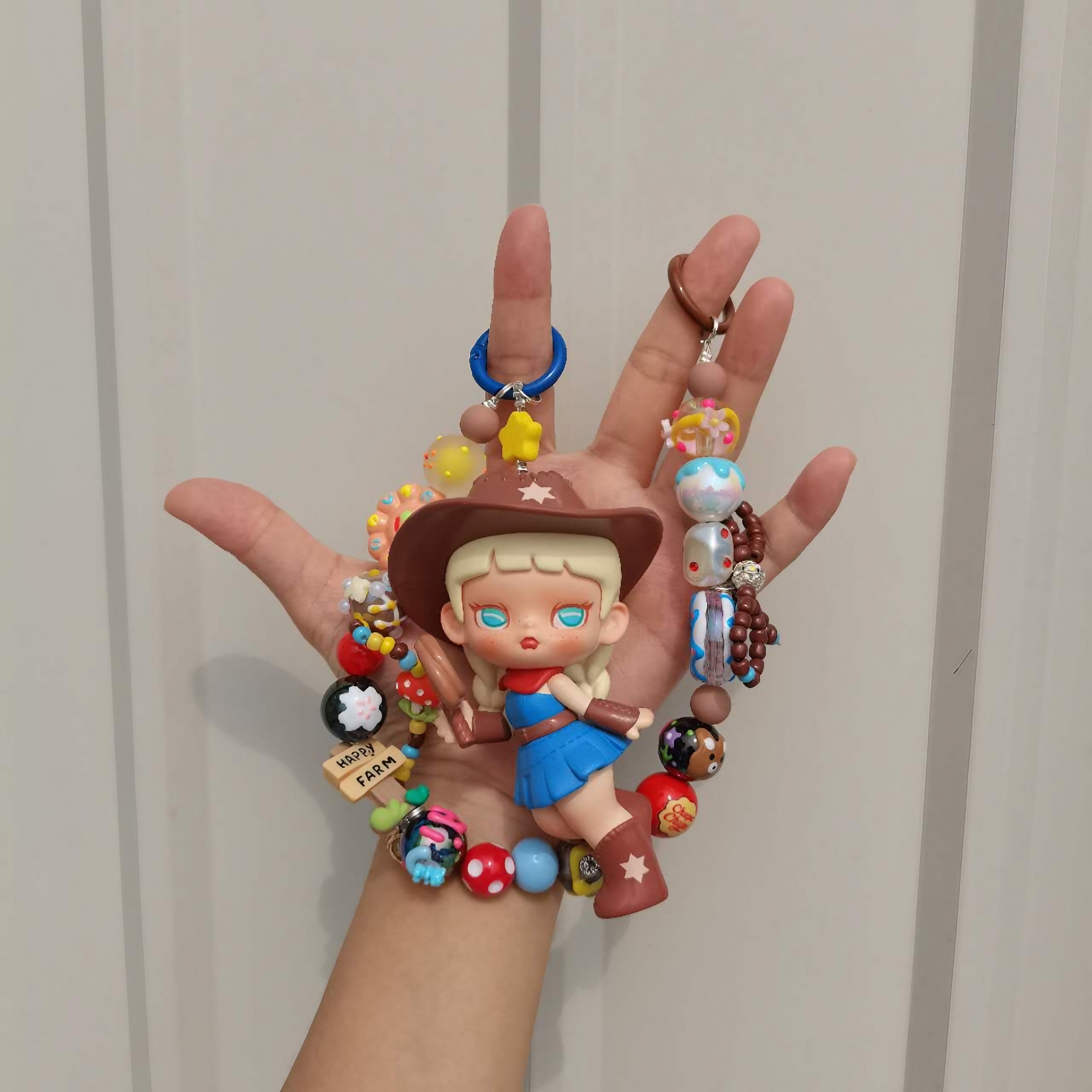 A hand displaying a kawaii cowboy keychain attached to a colorful bracelet