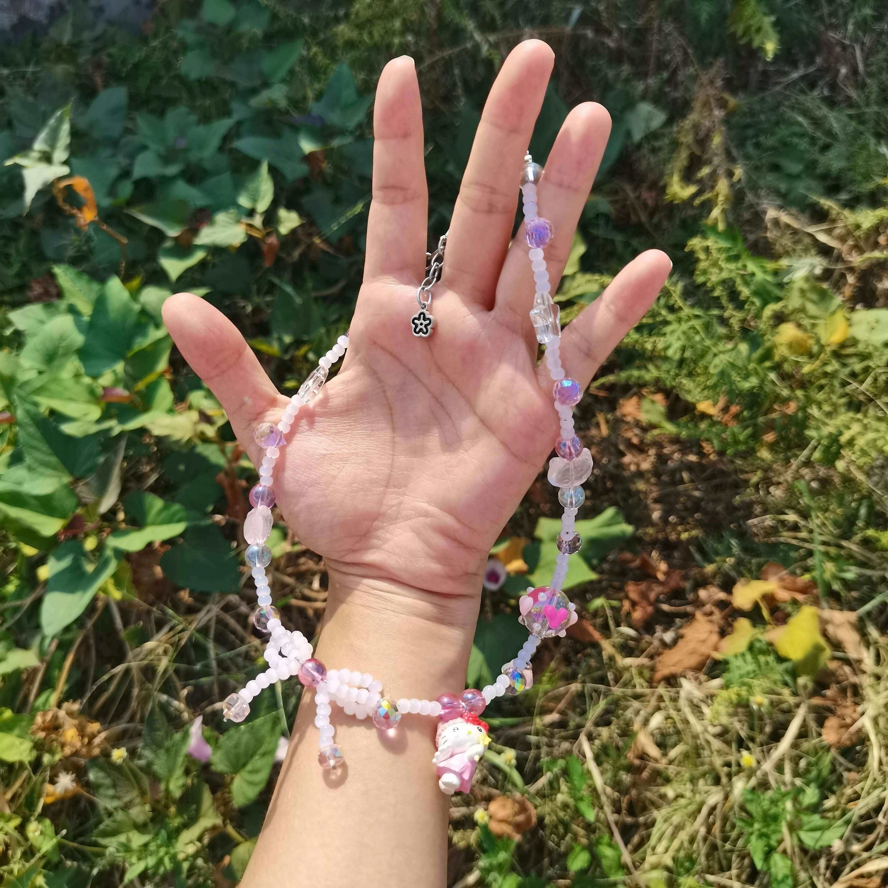 Close-up of a handmade pink beaded necklace with Hello Kitty charm in model's grasp