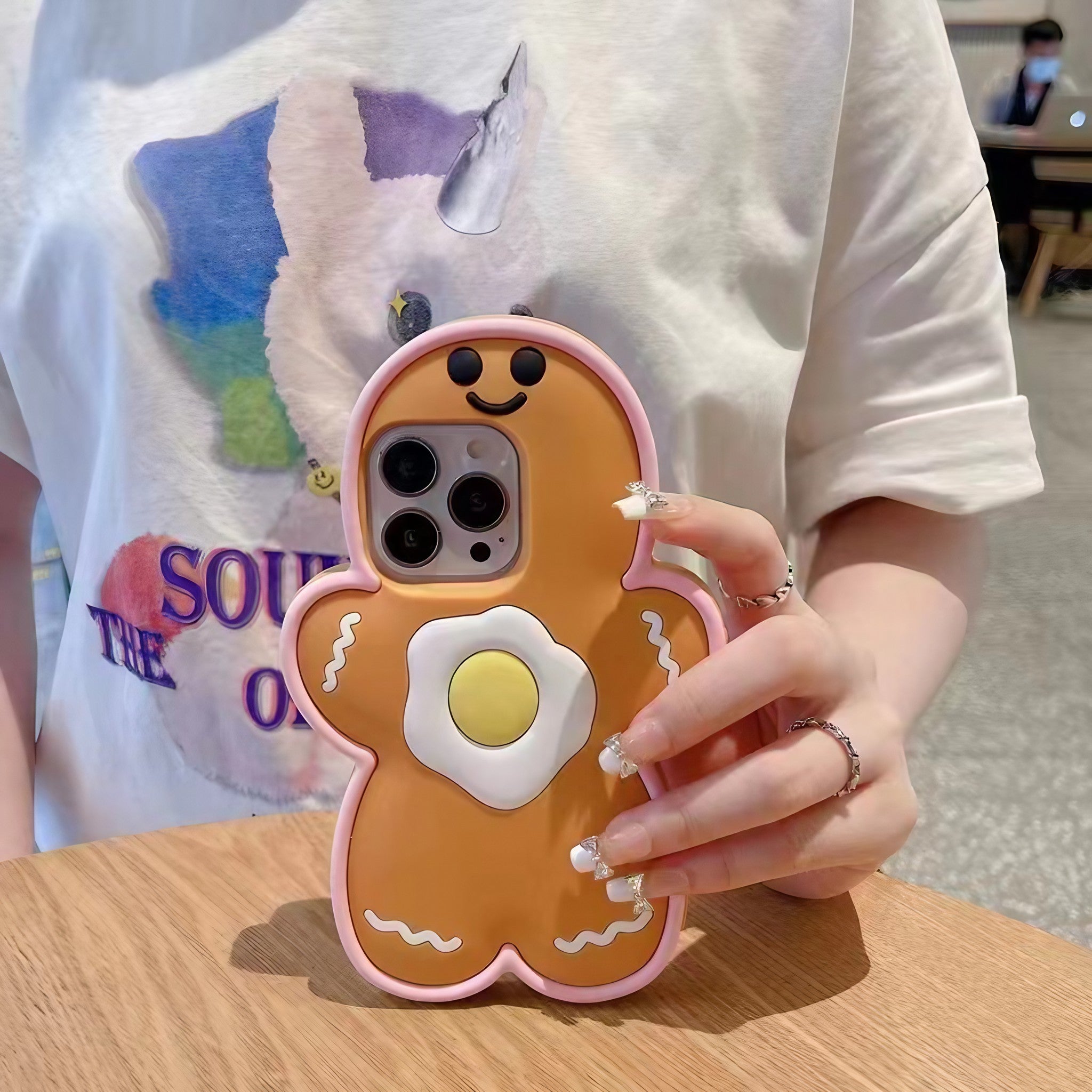 A woman's hand holding a festive gingerbread man iPhone case with a Y2K aesthetic