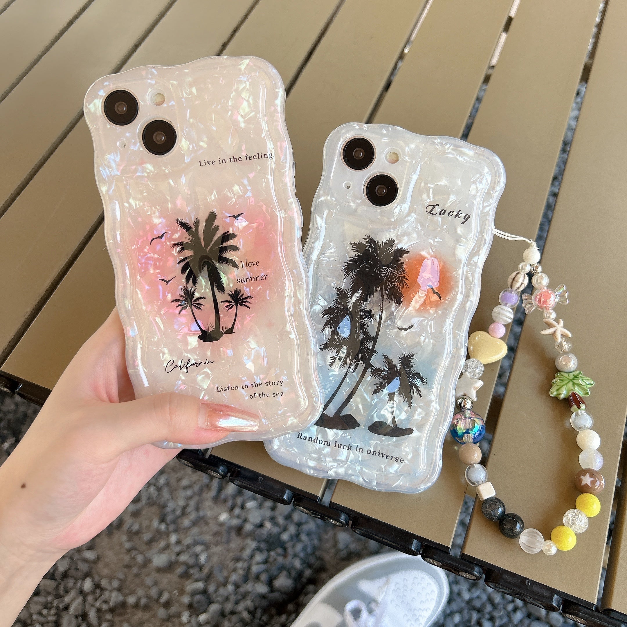 Two individuals showcasing an iPhone 14 series case featuring a summer sunset and coconut tree design with an attached phone chain