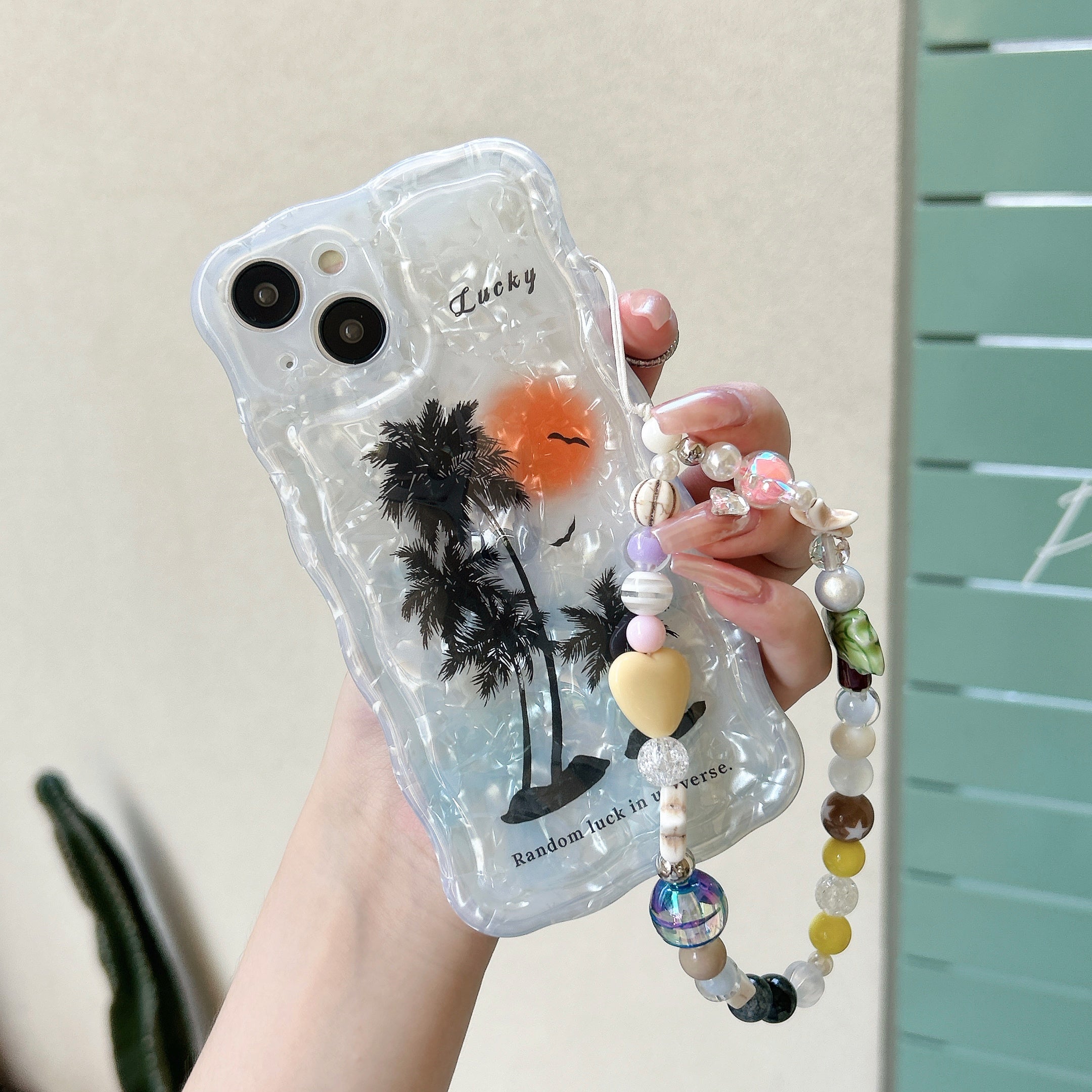 A close-up view of a person holding an iPhone case with a coconut tree design and decorative beads for a K-Pop inspired look