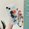 A close-up view of a person holding an iPhone case with a coconut tree design and decorative beads for a K-Pop inspired look