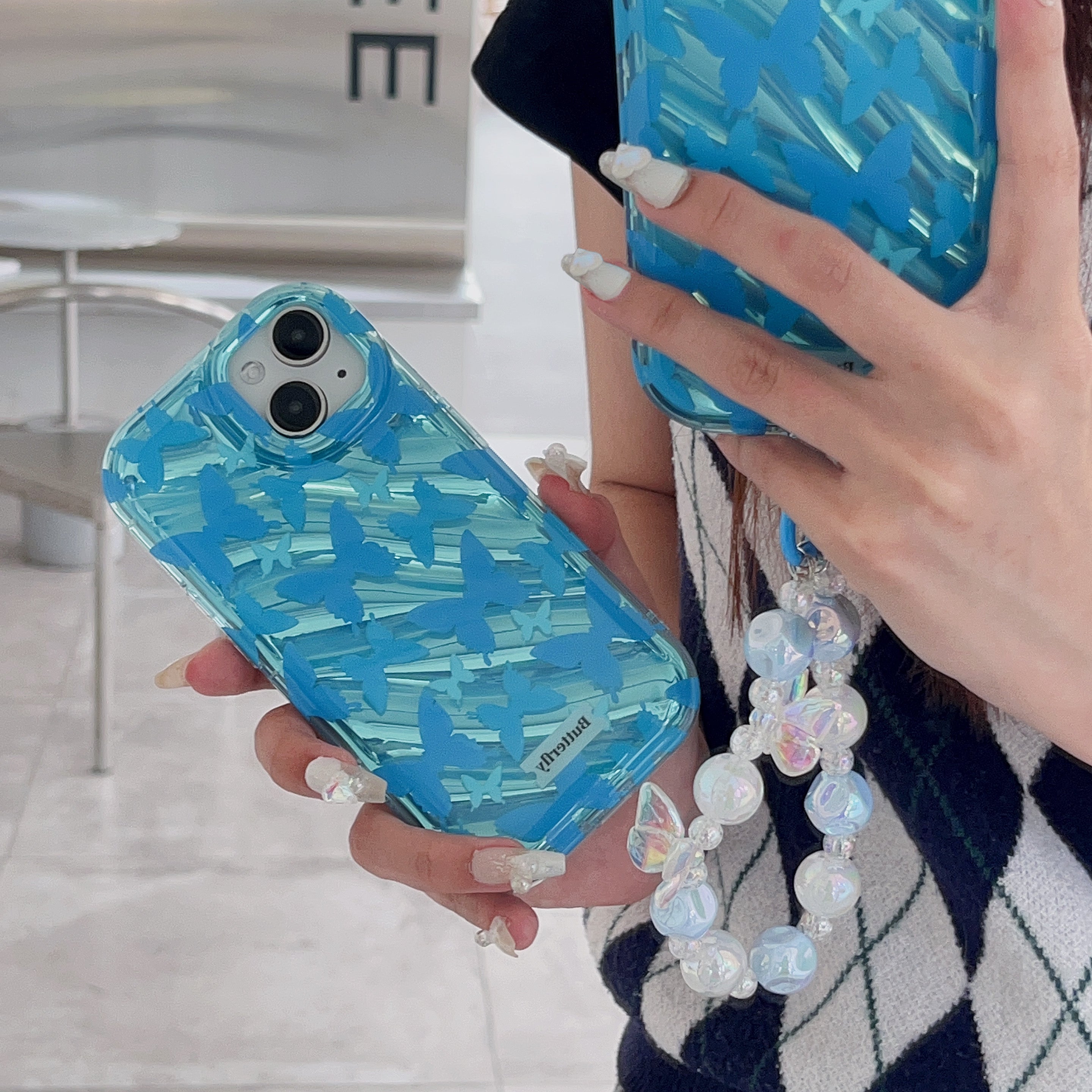 A woman presenting a pair of ice blue iPhone cases, each with an elegant phone chain accessory