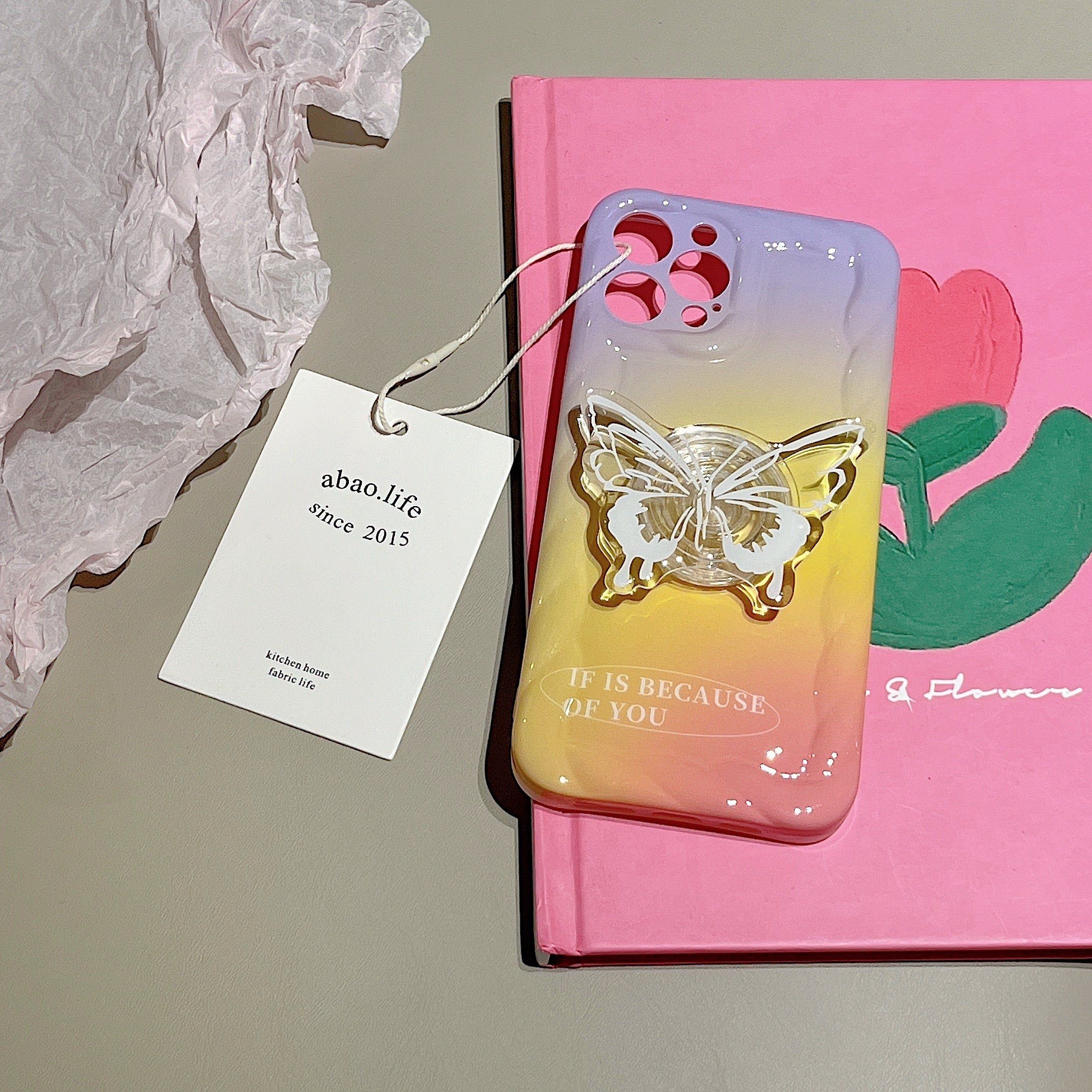 A pink notebook beside a coquette-style pink iPhone case with butterfly embellishment