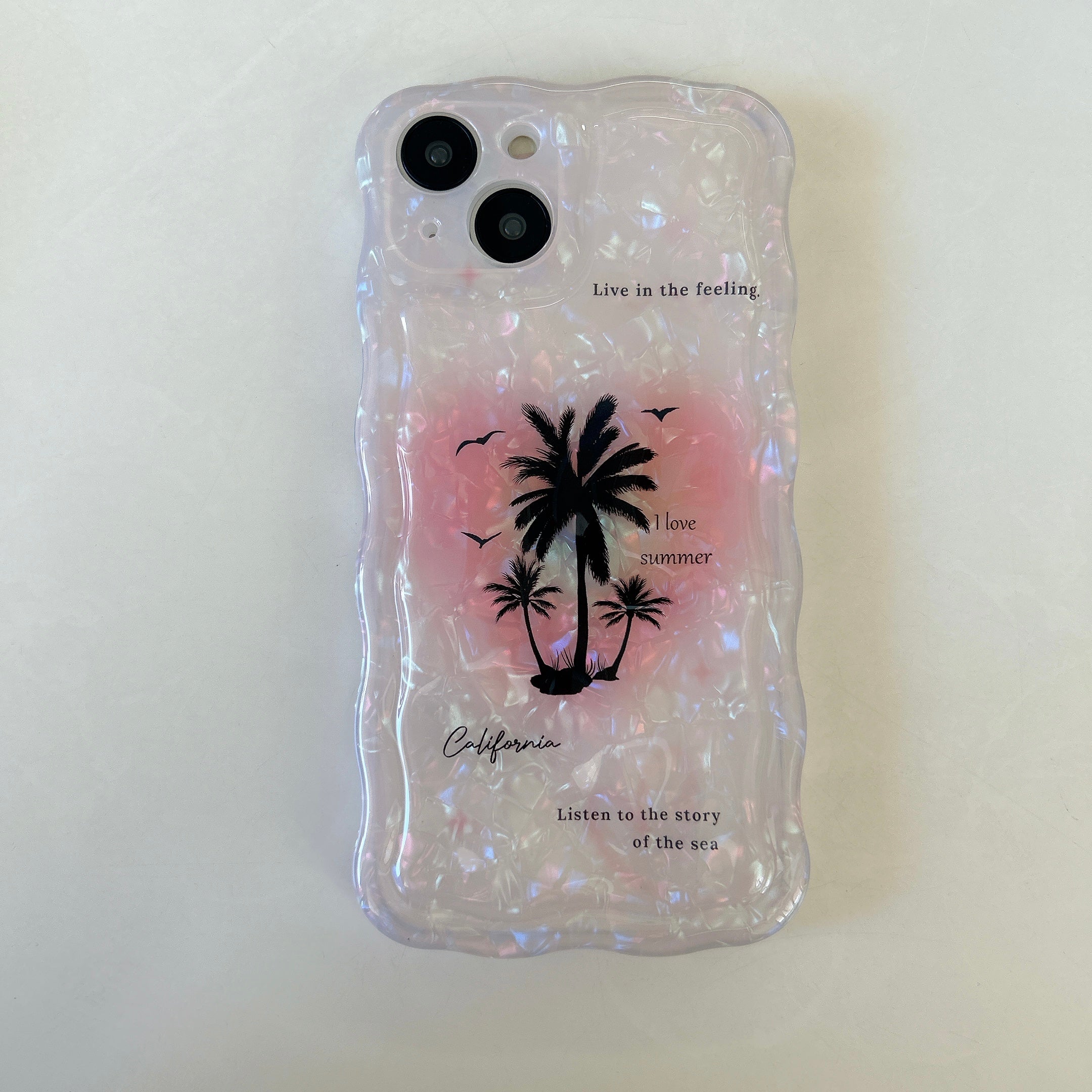 A clear iPhone case embellished with a coconut tree design and pink sparkles suitable for the iPhone 14 Pro